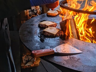 Flame-Grilled Cheeseburgers on Outdoor BBQ Grill with Melting Cheese and Spatula Near Open Fire