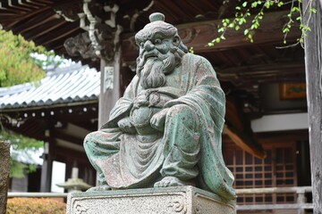 Ancient stone statue of a wise figure at a tranquil temple garden during a serene afternoon