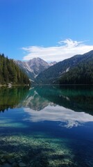 Fototapeta premium Serene mountain lake reflecting towering peaks and lush forests under a clear blue sky