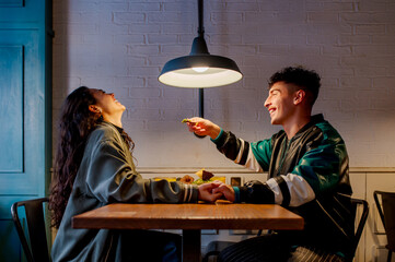 young Caucasian man offers food to his girlfriend as they dine together in a restaurant on a date. Boyfriend and girlfriend having a good time together.