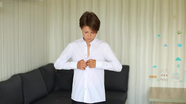 a teenage boy is shown in a close up as he prepares to wear a white school shirt. He carefully unbuttons the shirt and slides it over his arms. Moment in a teenager daily life
