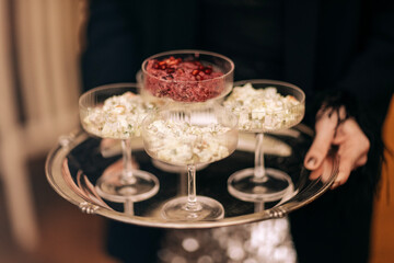 Close-up of a female hands with a neat manicure with a metal tray with four glasses of salads in a restaurant. Tasty snacks in elegant long-legged cremans.