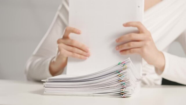 Woman sitting at office desk sorting overload stack of paper documents with colorful paper clips. Bureaucracy business concept.
