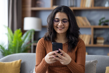 Close-up photo of a young Indian girl at home, holding a mobile phone and smiling at the screen