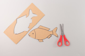 The fish cut out is placed below the cardboard, and the scissors are positioned to the right of the...