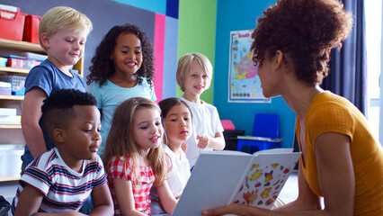 Group Of Elementary School Pupils Sitting On Floor Listening To Female Teacher Read Story
