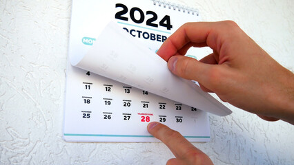 Close-up of male hands pointing finger at Thanksgiving 2024 date on the page of a wall calendar