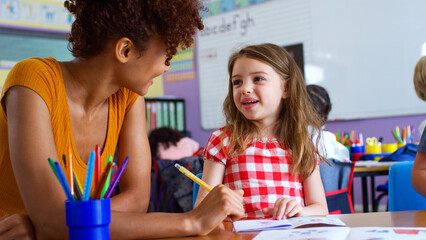 Female Elementary School Teacher Giving Female Pupil One To One Support In Classroom 