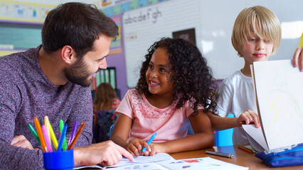 Male Elementary School Teacher Giving Female Pupil One To One Support In Classroom 