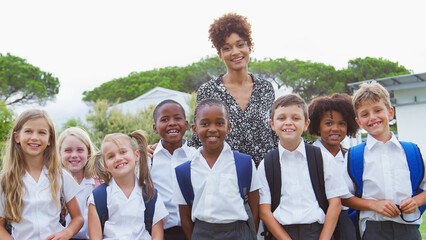 Outdoor Portrait Of Elementary School Pupils With Teacher Wearing Uniform Standing On Playing Field