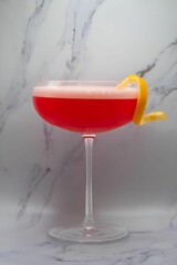 Glass of Aperol gin cocktail with twisted lemon on a white  marble background