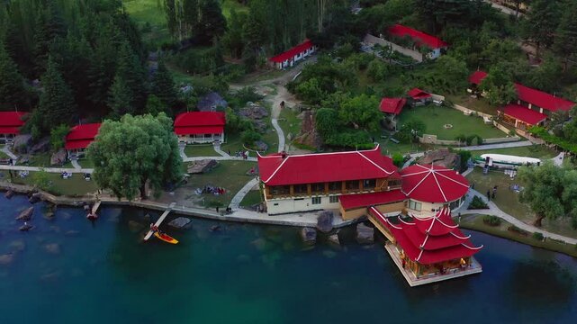 Drone shot over a Skardu city with red roof houses and green trees around lake in Pakistan