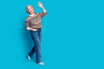 Full length photo of cheerful senior person wear ornament pullover waving palm say hi walk empty space isolated on blue color background © deagreez