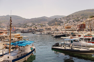 The vibrant harbor of Hydra is bustling with boats anchored alongside picturesque buildings, revealing the island's stunning landscape under a clear sky.