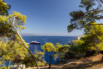 The Hydra boat port showcases a vibrant catamaran floating in sparkling waters, surrounded by greenery and distant mountains beneath a bright sky.