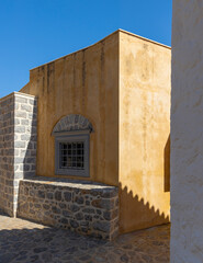 The warm hues of Hydra's traditional houses blend beautifully under a clear blue sky. Unique architectural details and stonework add character to this picturesque setting.