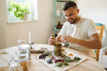 Handsome bearded man adds dried herbs to a mortar and pestle. Homemade healthy and nutrition...