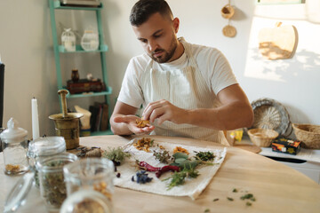 Handsome man in an apron sits at the table and preparing healthy and nutrition herbal tea