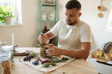 Process of man grinds various spices and dried herbs in a mortar and pestle.