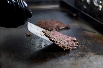 Hand using a spatula to flip cooking smash burgers on a grill in a restaurant kitchen