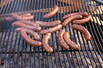 Close-up of large beef sausages being grilled on an open grill with a grate.