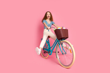 Joyful woman riding a bicycle on a vibrant pink background