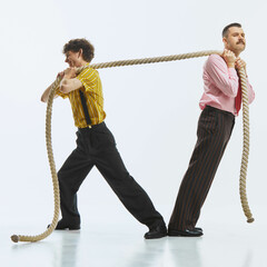Two men engaged in tug of war, one pulling rope with all his strength while other in resistance, showing competitive spirit. Concept of teamwork challenge, retro style, lifestyle situation.