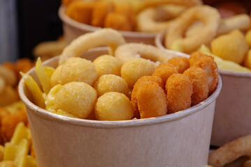 Fried potatoes, cheese fried balls and other baked goods in large paper bowls