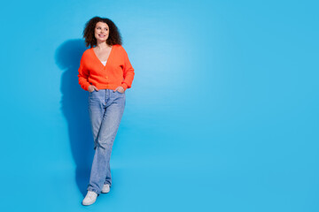 Photo portrait of wavy haired model woman wearing orange cardigan and jeans looking for new outfit isolated on blue color background