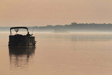 Silhouette of a man fishing in a pontoon boat on the early morning river.