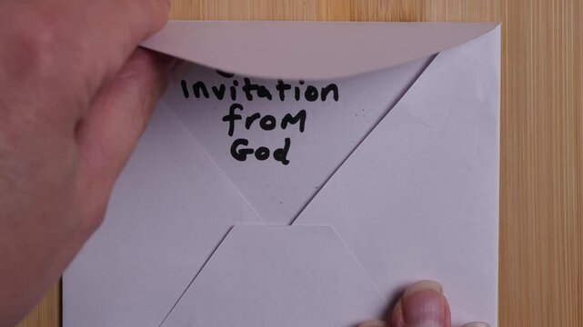 A person is opening a white envelope that contains a white card. On the card are written the words Your Invitation from God. Concept, religion, Christianity, salvation, evangelism. Slow motion.