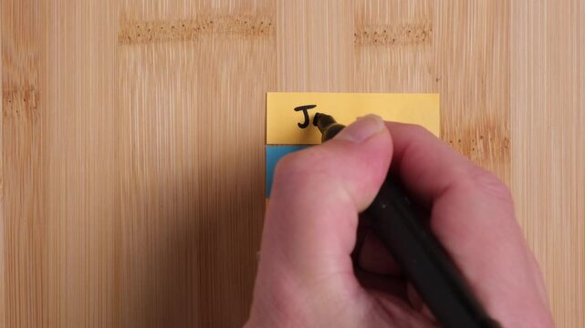 A person is writing on sticky notes on a wooden background. The person is writing Jesus Loves You. Concept, religion, Christianity, love.