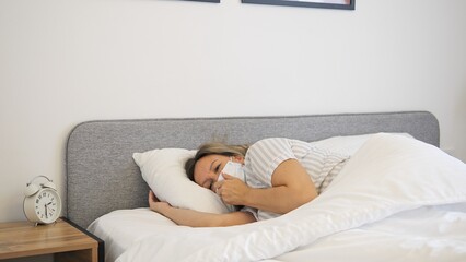 A woman in a mask lies in bed suffering from illness. The scene conveys fatigue and vulnerability, reflecting the impact of illness. Ideal for themes related to recovery, health and disease management