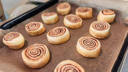 Step-by-step process for making cinnamon rolls, twisted synabons fit dough on deco with baking paper, side view. Cinnamon roll background. Close-up of homemade sweet pastry made from yeast dough.
