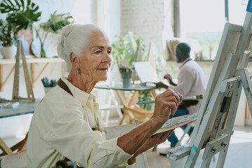 Medium close up of senior refined woman painting on canvas in drawing studio during her art therapy attendance