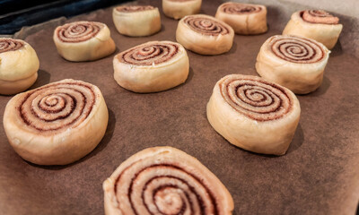 Step-by-step process for making cinnamon rolls, twisted synabons fit dough on deco with baking paper, side view. Cinnamon roll background. Close-up of homemade sweet pastry made from yeast dough.