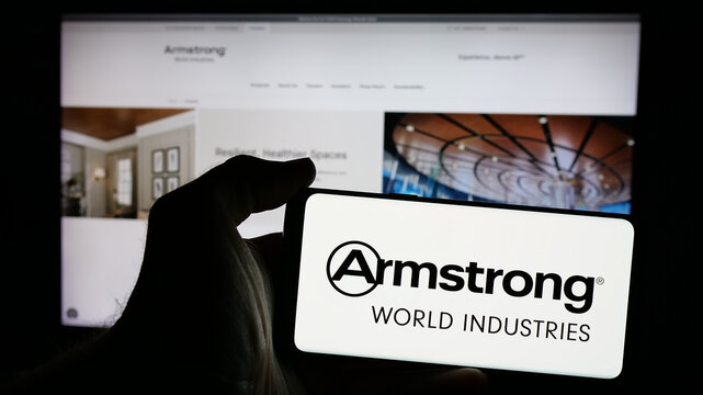 Stuttgart, Germany - 10-08-2024: Person holding smartphone with logo of US company Armstrong World Industries Inc. on screen in front of website. Focus on phone display.