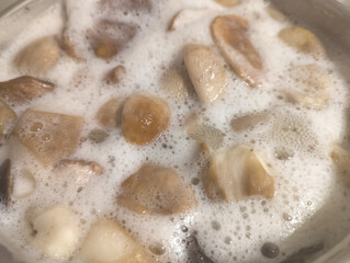 Beautiful small porcini mushrooms are boiling in a saucepan. Autumn mushroom season.