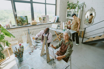 High angle shot of vintage drawing studio with young adult drawing tutor and group of elderly...