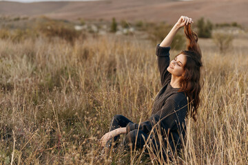 Serene woman sitting in a meadow with windblown hair against a majestic mountain backdrop