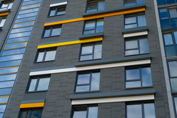 A close-up view of a modern apartment building with black brick and yellow accents, showcasing the sleek design of the windows
