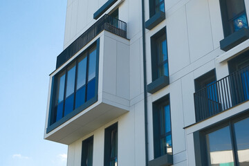 A modern white building with large windows and balconies against a clear blue sky