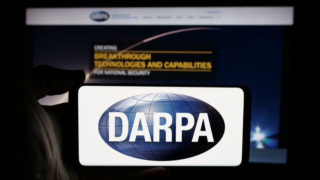 Stuttgart, Germany - 2024-10-10: Person holding cellphone with logo of Defense Advanced Research Projects Agency (DARPA) on screen in front of webpage. Focus on phone display.