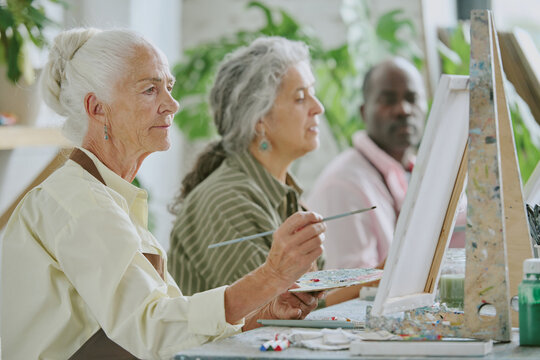 Medium close up of elderly friends visiting art session together, they drawing on canvas with oil paints