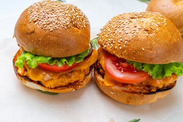 Juicy three burgers with beef patty, tomatoes, onions and lettuce on baking paper. on a light background
