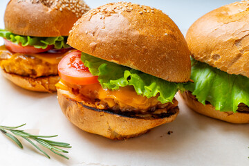 Juicy three burgers with beef patty, tomatoes, onions and lettuce on baking paper. on a light background