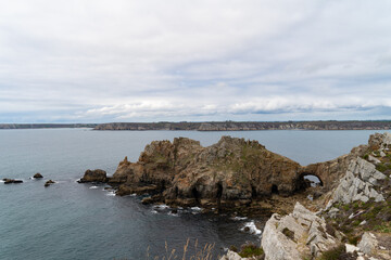 Le château de Dinan se dresse face à l’océan sous un ciel nuageux, les falaises majestueuses contrastant avec la lumière douce de l’été.
