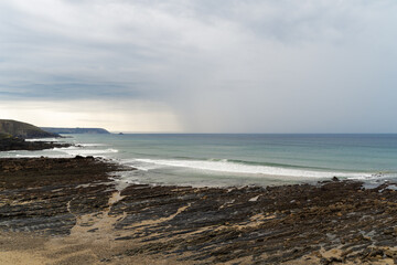 Un ciel gris s’étend au-dessus du site de la pointe de Dinan, tandis que les teintes automnales enveloppent les falaises dans une lumière tamisée, avec les sillons rocheux visibles à marée basse.