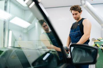 Muscular mechanic in uniform polish auto hood using grinding unit in automobile repair and renew service station. Repair after accident. Concept of professional car repair and maintenance work.