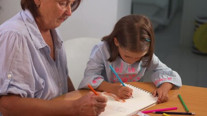 Focused grandmother and granddaughter coloring together in book on table at home. The scene is filled with creativity and warmth, as they bond over their artistic activity